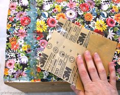 a person holding up a piece of brown paper next to a flowered table cloth