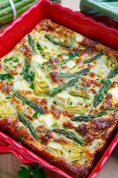 a red casserole dish with asparagus and cheese