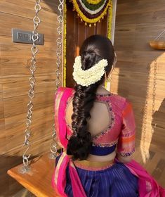 a woman sitting on top of a wooden bench wearing a pink and blue sari