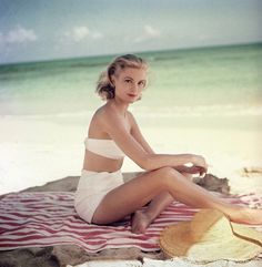 a woman sitting on top of a beach next to the ocean wearing a white bathing suit