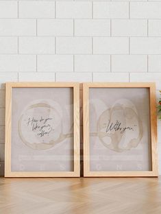 two framed art pieces sitting on top of a wooden table next to a potted plant