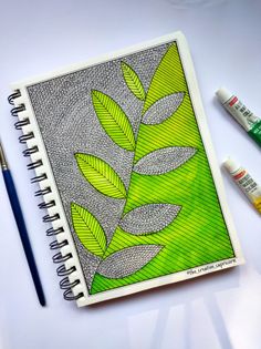 a spiral notebook with leaves on it next to markers