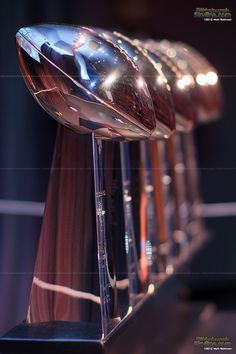 several shiny footballs are lined up on a table with their lights turned on in the background