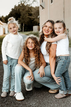 Mother and three children squatting on the ground in matching jeans and white tops