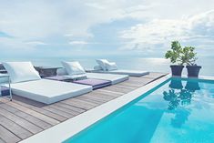 an outdoor pool with chaise lounges on the deck overlooking the water and sky