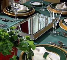 the table is set with green and gold plates, silverware, and greenery