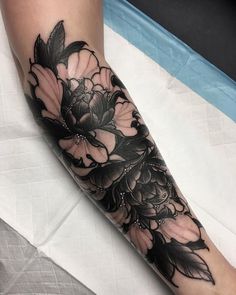 a woman's leg with flowers on it and black ink in the middle, sitting on a bed