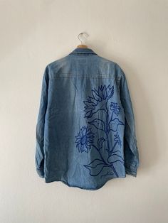 a denim jacket with blue flowers on it hanging from a hook in a white wall