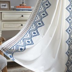 a blue and white blanket hanging from a bed next to a dresser with books on it