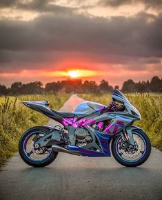 the motorcycle is parked on the side of the road near tall grass as the sun sets