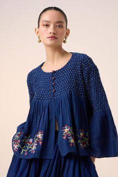 Blue top with smocked yoke top, embroidered buttons and contrast floral embroidery on the hem. - Aza Fashions Blue Cotton Blouse With Smocked Cuffs, Indigo Long Sleeve Tops With Floral Embroidery, Long Sleeve Indigo Tops With Floral Embroidery, Indigo Cotton Top With Floral Embroidery, Blue Folk Style Top With Embroidered Hem, Blue Folk Style Tops With Embroidered Hem, Indigo Cotton Tops With Floral Embroidery, Folk Style Blue Tops With Embroidered Hem, Blue Cotton Embroidered Hem Top