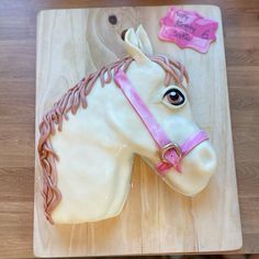 a cake shaped like a horse is on a wooden board with pink ribbon around its neck