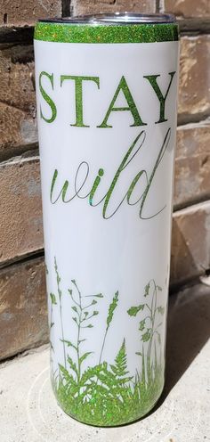 a white and green tumbler with the words stay wild painted on it's side