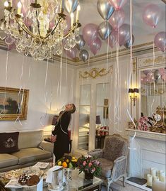 a woman standing in a living room filled with furniture and balloons hanging from the ceiling