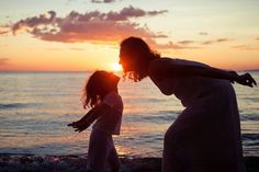 a mother and daughter playing on the beach at sunset