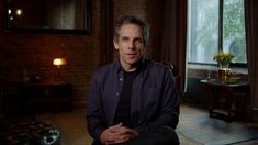 a man sitting in a chair with his hands crossed and looking at the camera while wearing a black shirt