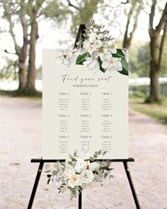 a sign with flowers and greenery is displayed on a tripod in the park