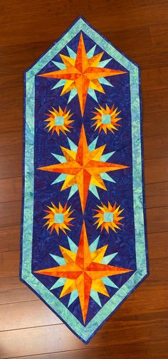 a blue and orange quilt on a wooden floor with a pattern in the center that looks like starbursts