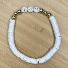 a white beaded bracelet with gold beads and words written on the clasp, sitting on a wooden surface