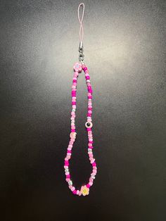 a pink and white beaded necklace hanging from a hook on a black background,