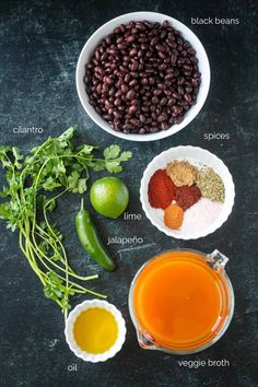 ingredients to make black bean soup in bowls on a dark surface with green beans, cilantro, limes and spices