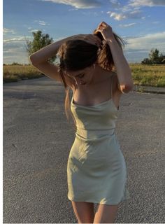 a woman standing in the middle of an empty road wearing a tan dress and heels