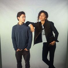 two young men standing next to each other in front of a white background, one wearing a black jacket