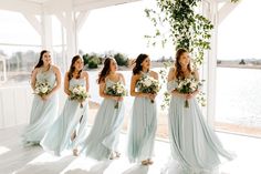 a group of women standing next to each other in front of a window holding bouquets