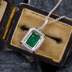 This elegant necklace features a slide pendant accented with one (1) emerald cut emerald set into four prongs. The pendant is accented with twenty-nine (29) prong set round brilliant cut diamonds. The pendant measures 17.8mm by 9.1mm. The 14k white gold pendant is suspended from a 16 inch long, 14K white gold cable chain. Formal Hallmarked Emerald Necklace, Fine Jewelry With Rectangular Pendant For Formal Occasions, Classic Emerald Pendant Necklace With Diamond Cut, Classic Diamond Cut Emerald Pendant Necklace, Classic Emerald Diamond Cut Pendant Necklace, Classic Jewelry With Emerald Cut Bezel Setting, Classic Diamond Cut Emerald Necklace For Formal Occasions, Classic Emerald Cut Jewelry With Bezel Setting, Classic Emerald Necklace With Diamond Cut For Formal Occasions