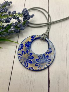 a blue and white flowered circle hanging from a cord on a wooden table next to purple flowers