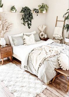 a bed with white sheets and pillows in a bedroom next to two potted plants