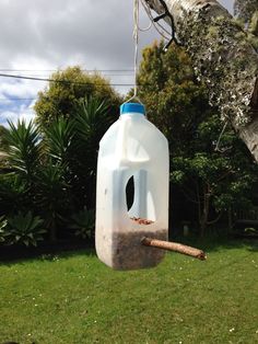 a plastic jug hanging from a tree with a bird feeder on it's side