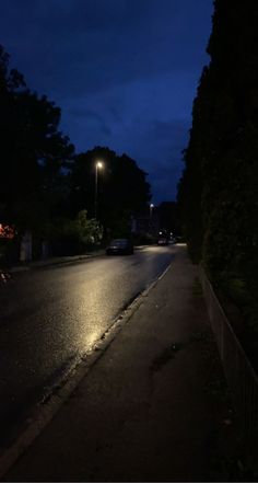 an empty street at night with cars parked on the side and trees lining the road