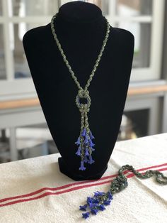 a necklace with purple flowers on it sitting on a mannequin head stand next to a beaded chain