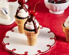 three ice cream cones with cherries and chocolate toppings on them, sitting on a red tablecloth