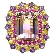 Ametrine, Pink and Yellow Sapphire 7.88 Carat Yellow Gold Cocktail Ring This ring definitely has a WOW factor! Flashing a vivid color of yellow and purple the vibrant Emerald Cut Ametrine sits between Yellow and Pink Sapphires and Diamond accents. Item Specs: Ametrine (Emerald cut stone) = 5.64 carats 14 Amethysts (Round Cut) = 0.86 carats 38 Yellow and Pink Sapphires (Round Cut) = 1.38 carats Total Carat Weight of the Ring = 7.88 carats 14KY Gold = 7.8 grams Ring size is 7 and can be re-sized at no additional cost Fun Facts about Ametrines: The ametrine stone is golden yellow and purple, something that happens when citrine and amethyst stones come into contact to form one crystal. This also gives the stone its name, derived from AMEthyst and ciTRINE. It is also referred to as bolivianite, Yellow Gold Cocktail Ring, Sapphire Cocktail Ring, Amethyst Stones, Jewelry Words, Purple Jewelry, Gold Cocktail Ring, Gold Cocktail, Diamond Cocktail Rings, Yellow And Pink