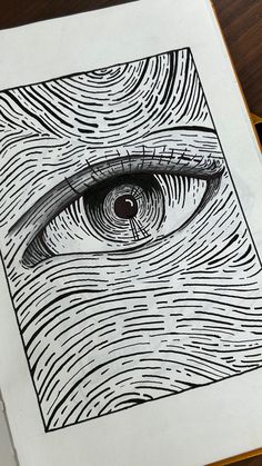 an eye drawn in black and white on top of a piece of paper next to a pen