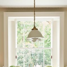 a kitchen sink under a hanging light in front of a window with potted plants