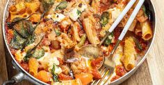 a pan filled with pasta and vegetables on top of a wooden cutting board next to a fork