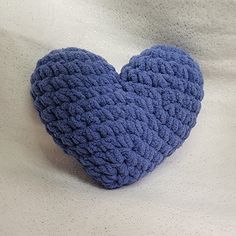 a blue crocheted heart sitting on top of a white sheet in the shape of a pillow