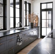 a kitchen with black counter tops and wooden floors, along with large windows that look out onto the street