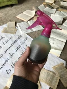 a hand holding a spray bottle with writing on the ground in front of it and papers scattered around