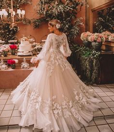 a woman in a white wedding dress standing next to a table with flowers and cake on it