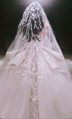 the back of a wedding dress with white flowers on it and veil over her head