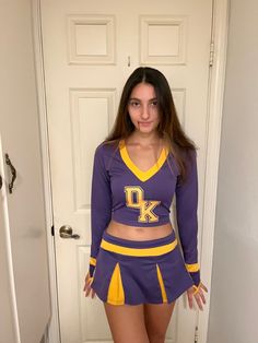 a girl in a purple and yellow cheerleader outfit posing for the camera with her hands on her hips