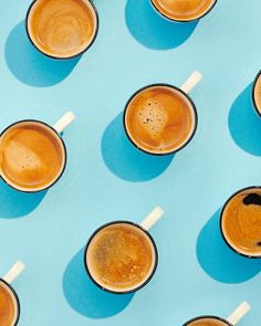 six cups of coffee are lined up on a blue surface