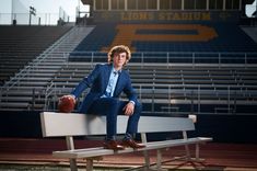 a man in a suit sitting on a bench with a football and stadium bleachers behind him