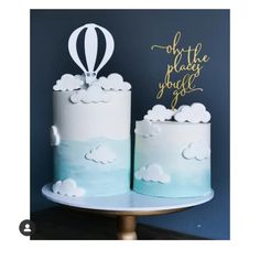 two cakes decorated with hot air balloons and clouds on a cake stand against a blue wall