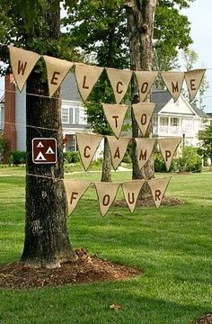 a welcome to camp sign hanging from a tree in front of a house on a lawn