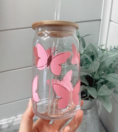 a person holding up a glass with pink butterflies on the inside and bottom, in front of a potted plant